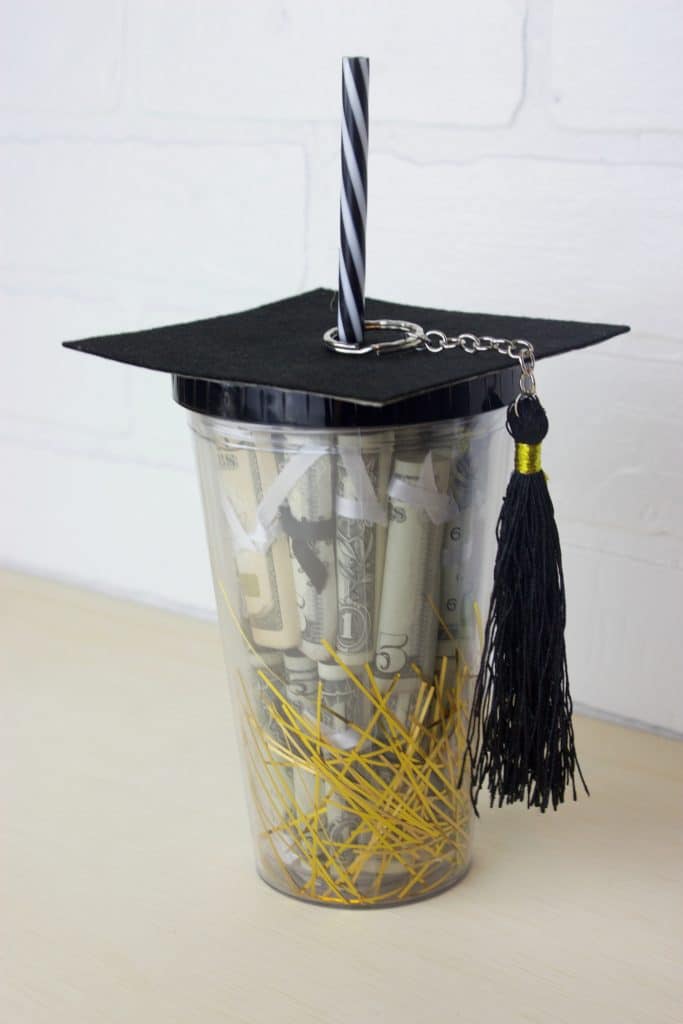 a jar filled with rolled up money and on top is a graduation hat covering the opening of the jar