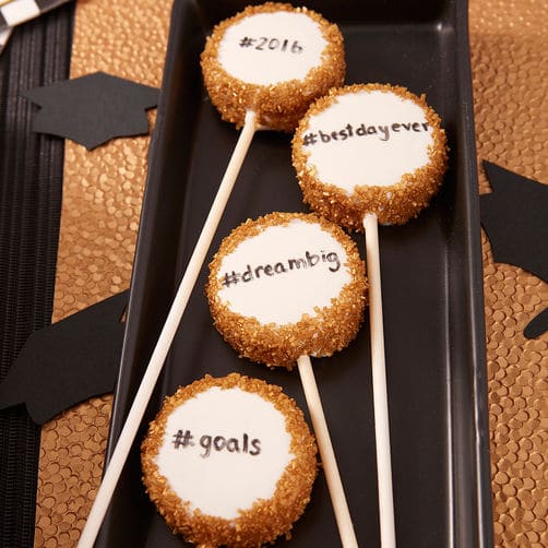 Graduation cake pops with different graduation sayings on each one on a black serving plate