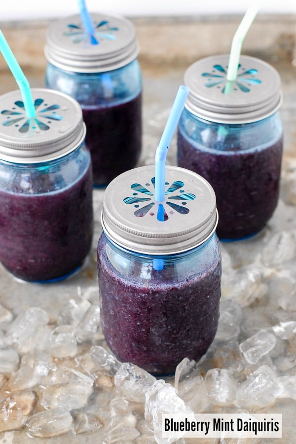 Blueberry mint daiquiris in jars with straws and it is sitting on ice