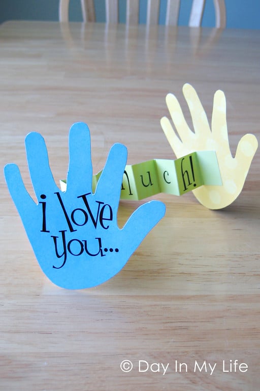 2 hand cut outs connected by a banner that says "I love you so much"