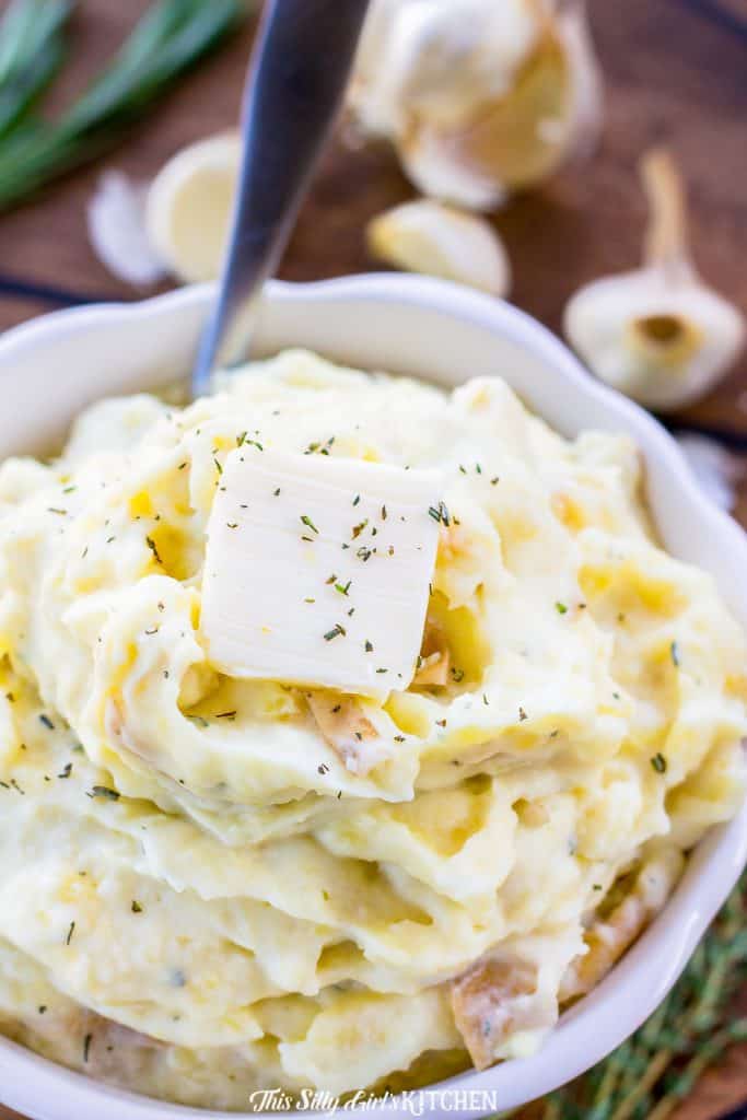 Roasted garlic mashed potatoes close up with butter on top in a white bowl