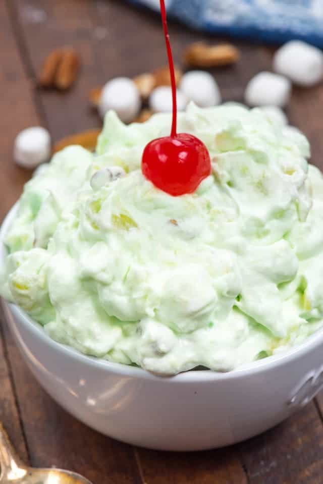 Watergate salad fluff in a white bowl with a cherry on top