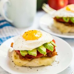 A side angle of the California Breakfast Stack showing the egg on top of the avocado slices, sliced tomato, bacon, cheese and english muffin.