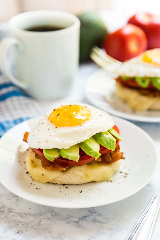 A side angle of the California Breakfast Stack showing the egg on top of the avocado slices, sliced tomato, bacon, cheese and english muffin.