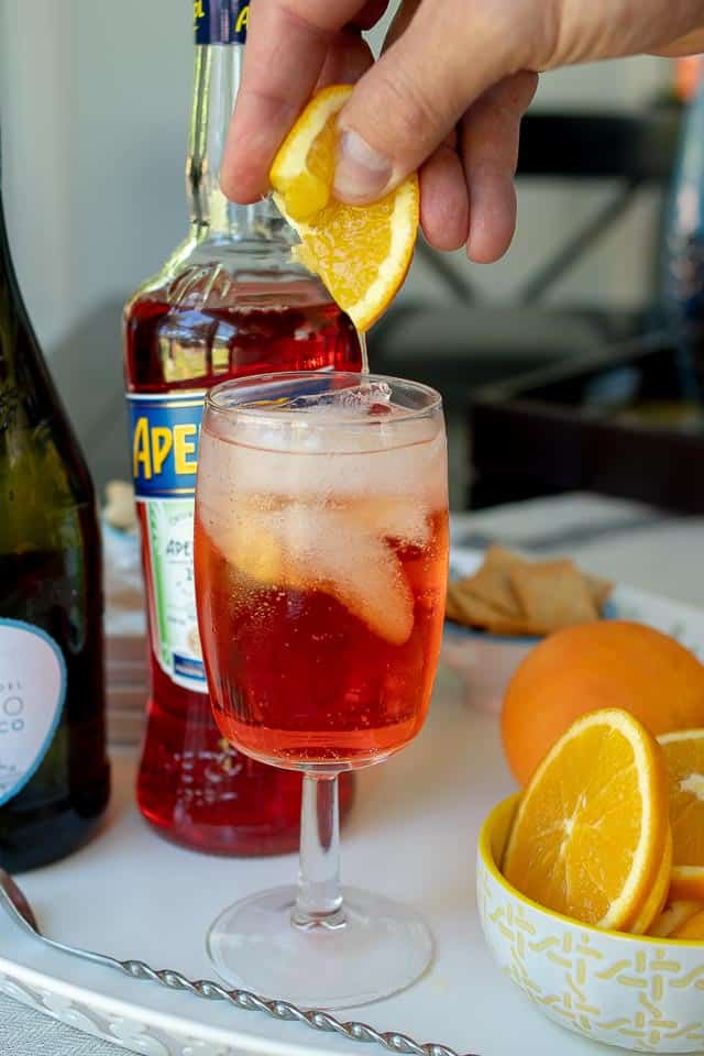 an orange wedge being squeezed into an Aperol spritz