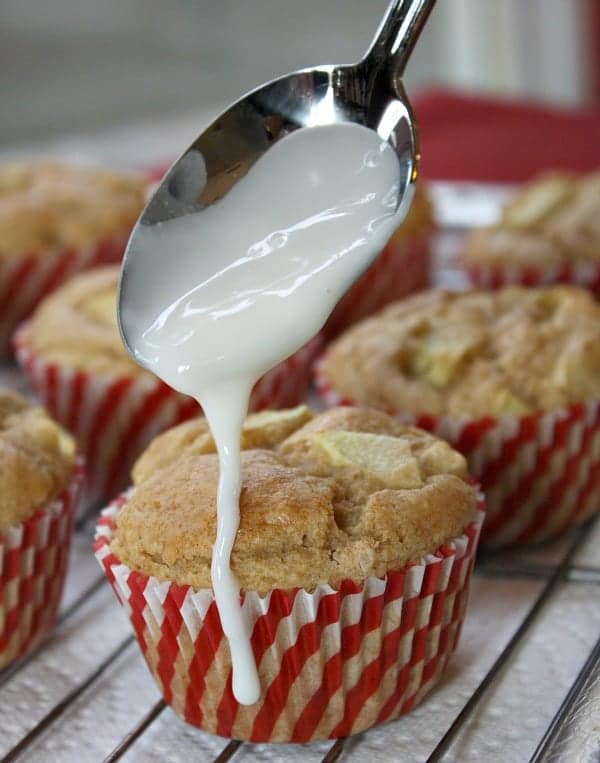 apple fritter muffins in red and white cupcake paper and frosting being poured on top