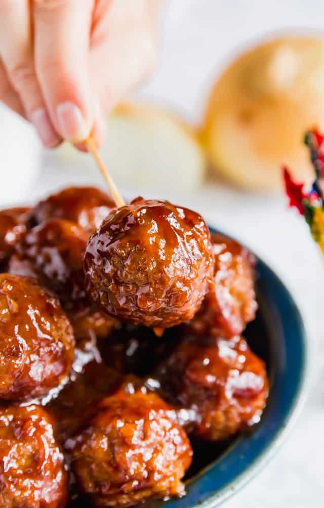 A hand holding a toothpick picking up a BBQ Meatball for a bowl of BBQ Meatballs.