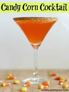 Candy Corn Cocktail in a martini glass with candy corn on the table below the glass with writing