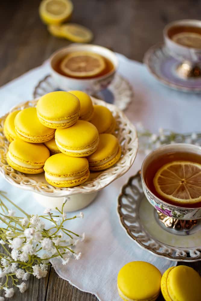 Lemon Macarons on white stand with three cups of lemon tea on a white cloth