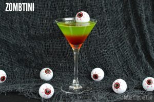 Zombtini cocktail with a fake eyeball floating in it and other fake eyeballs on the table below