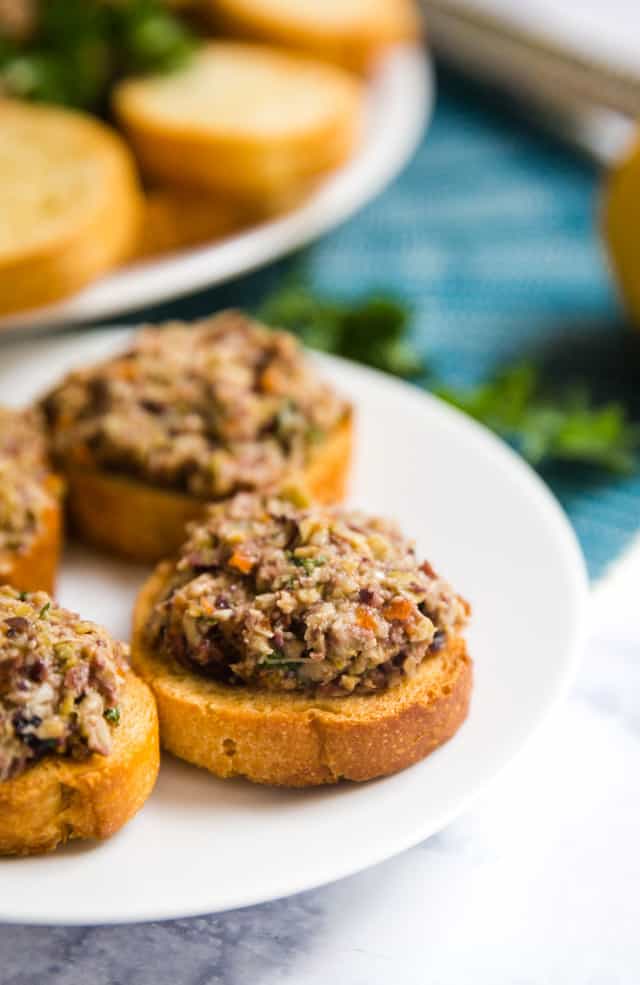Olive Tapenade on piece of toasted baguette on a white plate.
