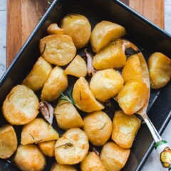 roasted potatoes in black oven tray on a wooden board