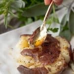 a small gold spoon spooning on browned butter onto the smashed potatoes