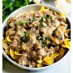 Beef and mushroom skillet in a white bowl served over noodles with recipe title on bottom of image