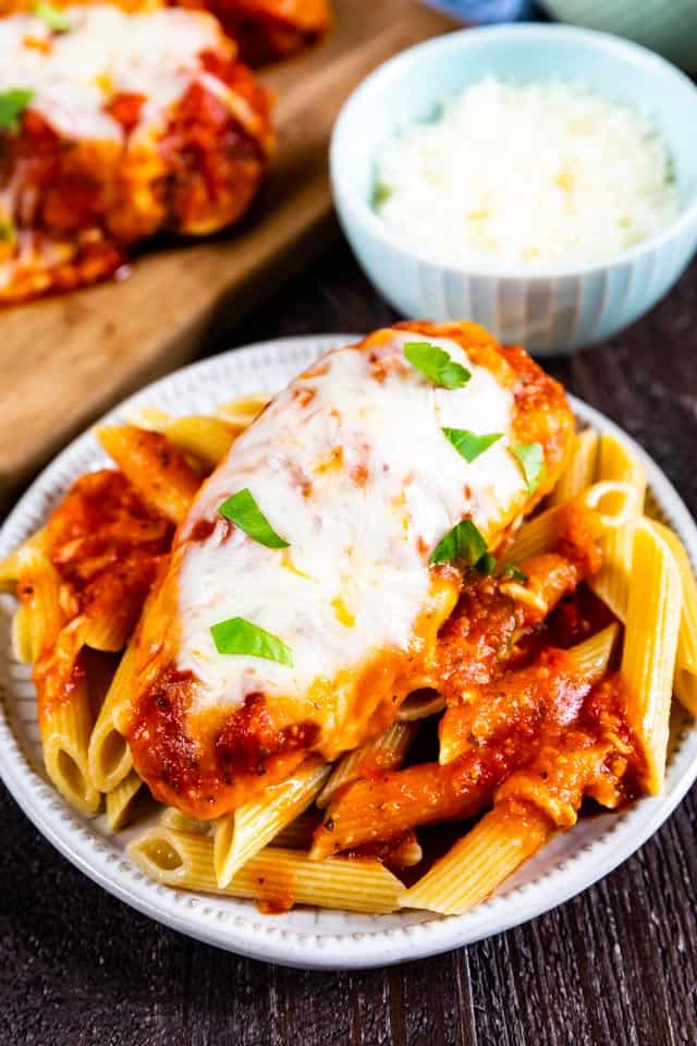 Crockpot chicken parmesan on top of penne pasta on a white plate