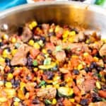 Mexican steak skillet in pan with ingredients behind it and recipe title on top of photo
