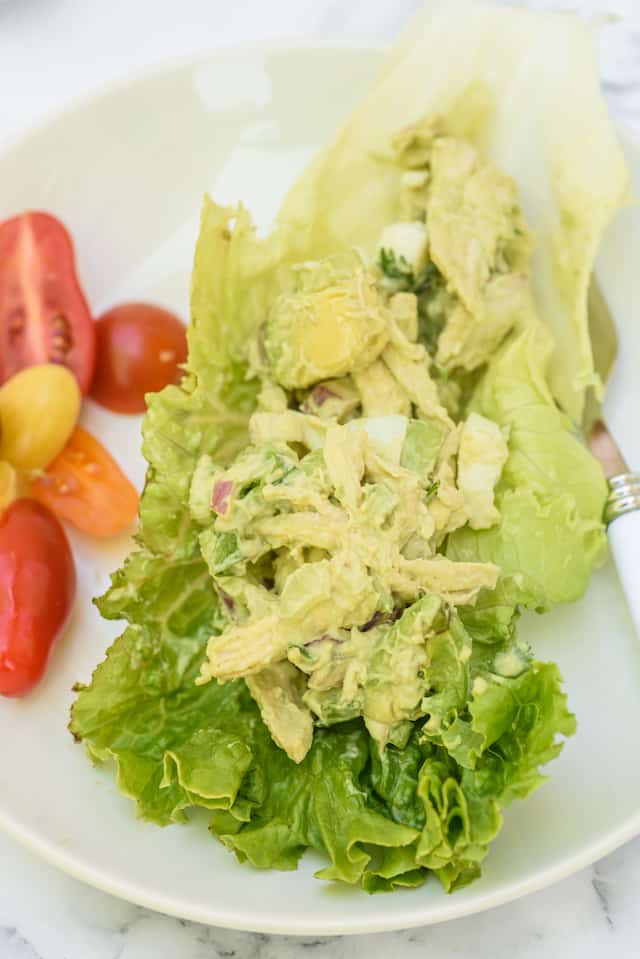 Close up shot of keto chicken salad in a lettuce wrap on a white plate with a side of cherry tomatoes