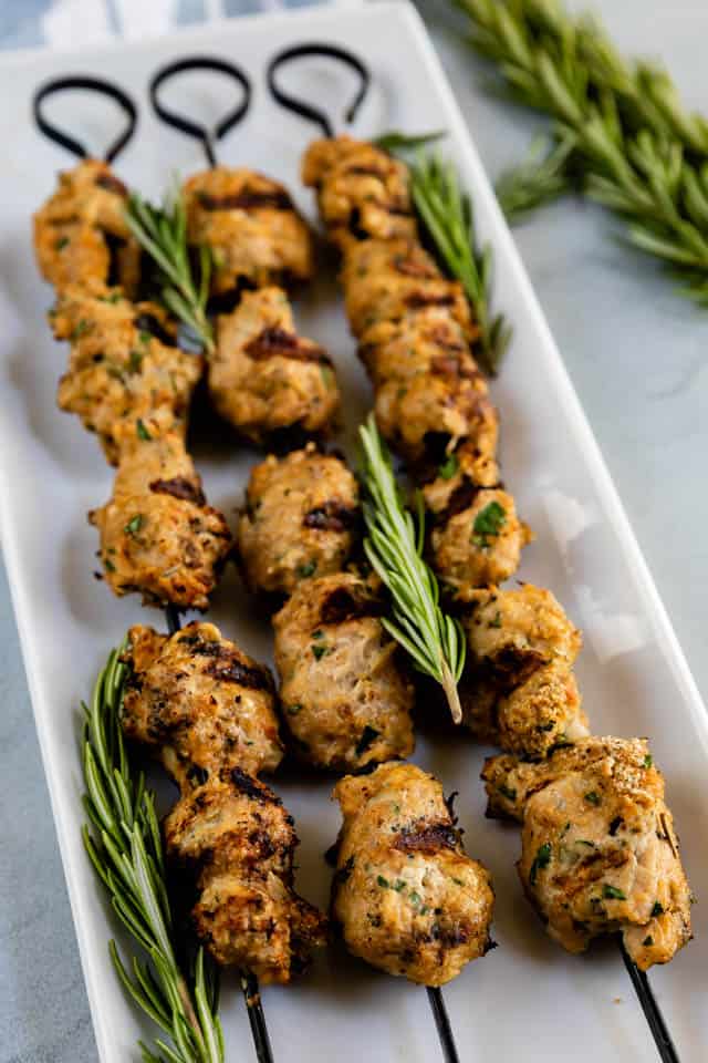 Three turkey kabobs on skewers on a white serving plate with rosemary