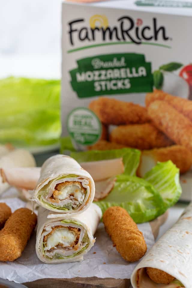 Easy turkey wraps on parchment paper with ingredients all around and mozzarella stick box in background