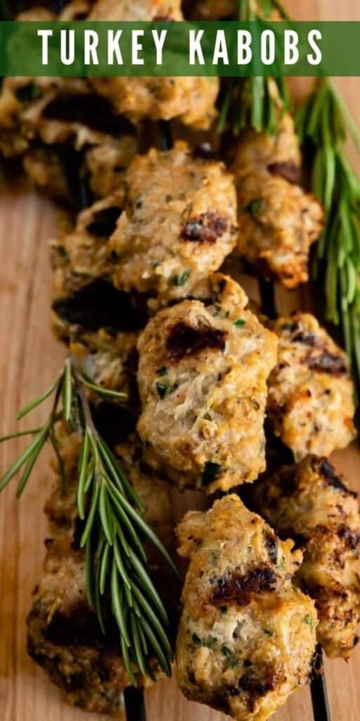 Turkey kabobs with rosemary on a wood cutting board with recipe title on top of image