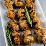 Three turkey kabobs on skewers on a white serving plate with rosemary with recipe title on bottom of photo
