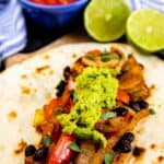 Vegetarian fajita with guacamole on top and salsa and limes in background