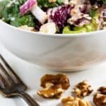 Apple walnut salad in a white bowl with silver fork and walnuts in front of it and recipe title on bottom of image
