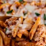 Baked penne casserole being scooped out of casserole dish with recipe title on top of image