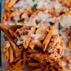 Close up of baked penne and sausage being scooped out of casserole dish with a wooden spoon