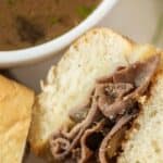 Close up shot of french dip sandwich cut in half on a plate with a side of au jus and recipe title on top of image