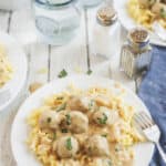 Overhead shot of swedish meatballs and egg noodles on a white plate with rest of table settings around it