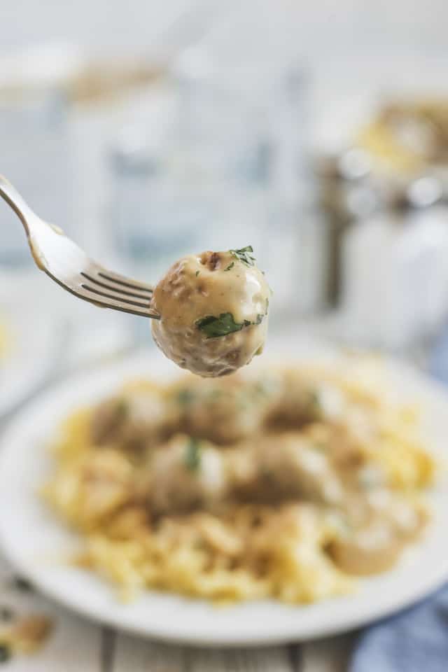 Close up shot of one swedish meatball on a fork in focus with rest of plated dinner behind out of focus