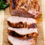 Overhead shot of pork tenderloin slices on a wood cutting board with recipe title on bottom of image