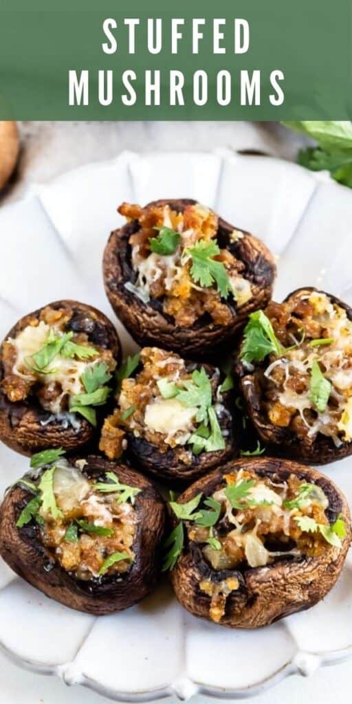 Overhead shot of 6 stuffed mushrooms on a white scallop plate with recipe title on top of image