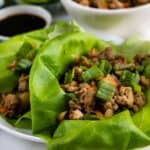 Close up shot of turkey lettuce wraps on a plate with extra ground turkey and sauce in background and recipe title on bottom of photo