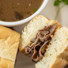 Close up shot of french dip sandwich cut in half on a plate with a side of au jus