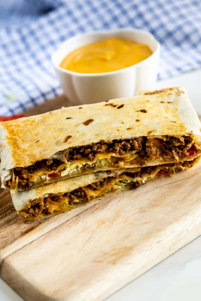 Copycat crunchwrap supreme cut in half and stacked on top of eachother with cheese sauce