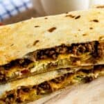 Copycat crunchwrap supreme cut in half and stacked on top of eachother with cheese sauce and recipe title on bottom of photo