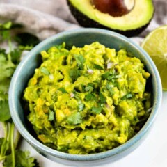 Bowl of fresh guacamole with avocado in background