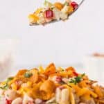 Spoonful of frito corn salad being lifted over the full bowl of salad with recipe title on top of image