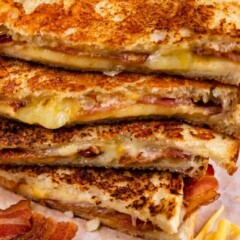 Grilled cheese sandwiches cut in half and stacked on top of eachother surrounded by cheese and bacon