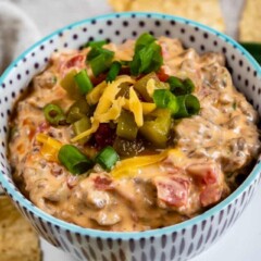 Bowl of sausage queso dip with toppings and tortilla chips around it