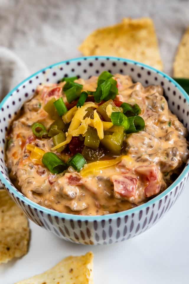 Bowl of sausage queso dip with toppings and tortilla chips around it