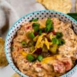 Bowl of sausage queso dip with toppings and tortilla chips around it and recipe title on top of photo