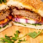 Barbecue turkey burger cut in half on wood cutting board surrounded by arugula with recipe title on bottom of image