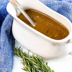 Brown gravy in a white gravy boat with thyme next to it