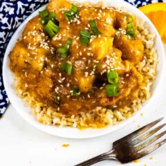 Overhead shot of orange chicken over rice in a white bowl with fork next to it