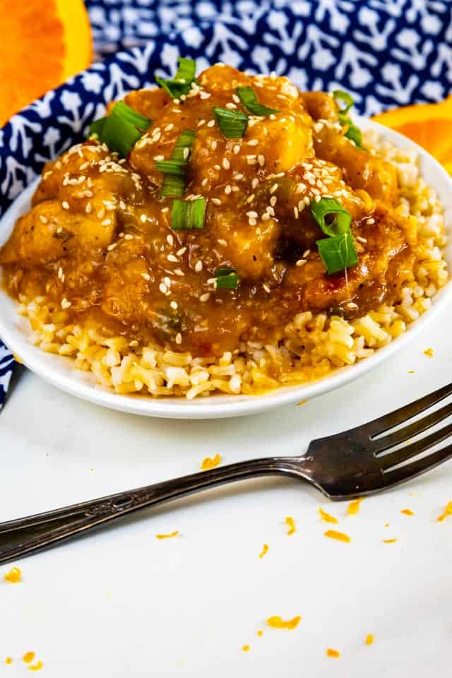 Overhead shot of orange chicken over rice in a white bowl with fork next to it