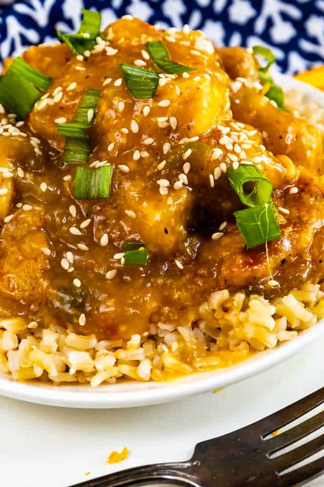 Close up shot of orange chicken served over rice in a white bowl