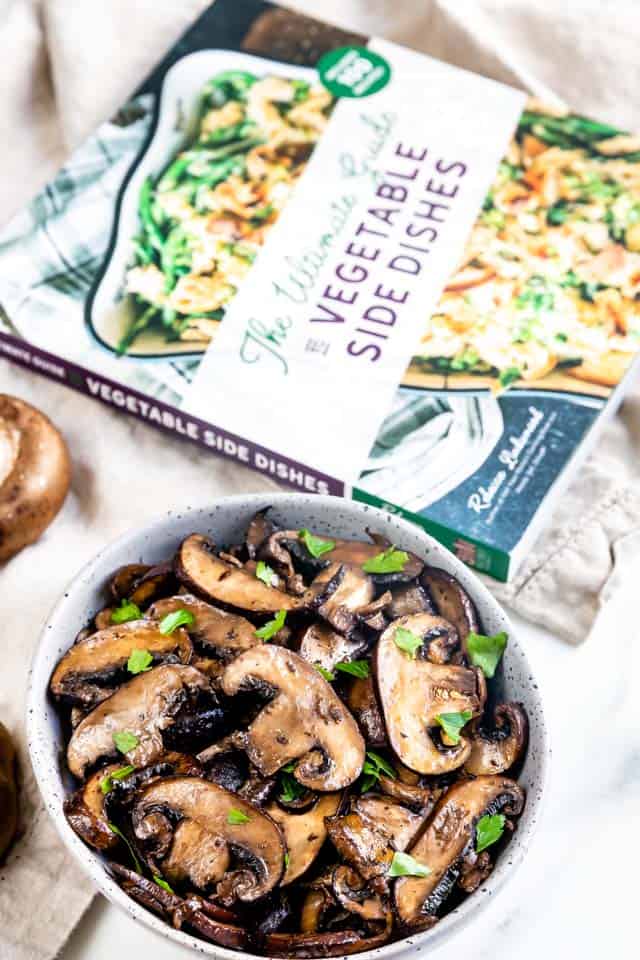 Overhead shot of oven seared mushrooms in a bowl next to a cookbook